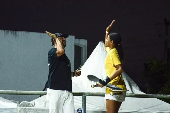 Lyliann comemorando com um skatista e segurando o skate
